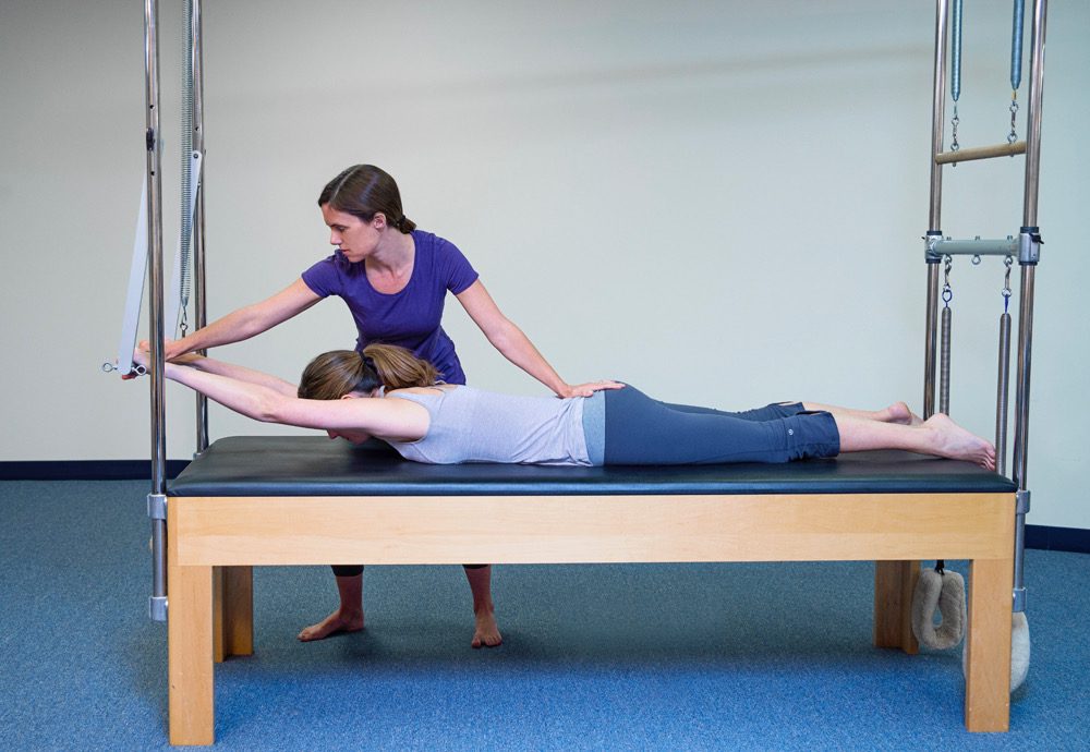 A woman is stretching on the bed while another person watches.